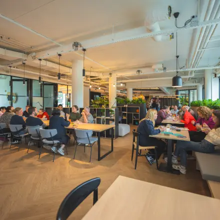 Office space rental in Den Bosch featuring an open floor plan at Hambakenwetering 1 with groups of people collaborating at tables.