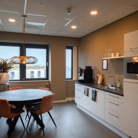 Modern office kitchen area at Keulenstraat 1, Deventer, available for office space rental, featuring a round table with chairs, microwave, and coffee machine.