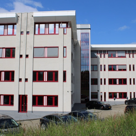 Exterior view of an office building for rent at Keulenstraat 1, Deventer, featuring a modern facade with red-framed windows and parking space in front.
