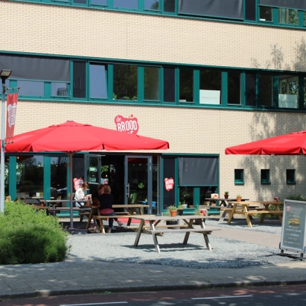 Exterior view of an office building at Keulenstraat 10, Deventer with outdoor seating under red umbrellas.