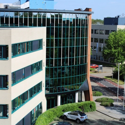 Exterior view of Keulenstraat 10 in Deventer, featuring a contemporary office building suitable for office space rental. The facade showcases large glass windows and a landscaped entrance area.