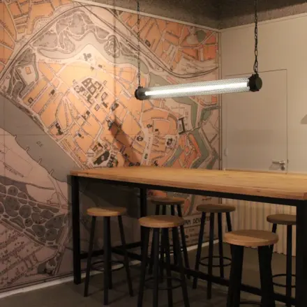 Modern office interior at Keulenstraat 12, Deventer featuring a large table, high stools, and a historic map mural. Ideal for those seeking office space rental with character.