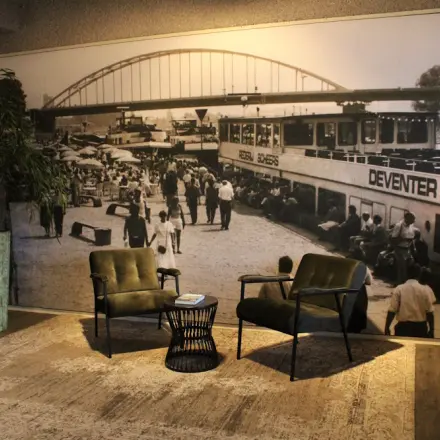 Office space rental at Keulenstraat 12, Deventer featuring a cozy lounge area with two chairs, a small table, and a large wall mural depicting a historical scene.