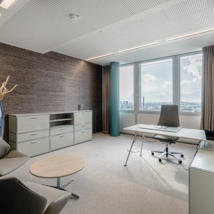Bright, stylish furnished office at Dreischeibenhaus 1, Düsseldorf Old Town with a large window view, modern desk, and comfortable chairs. Perfect for your next office space rental.