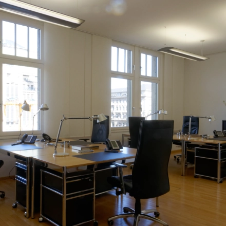 A furnished office to rent at Königsallee 14, Düsseldorf Old Town, featuring multiple desks, chairs, and ample natural light through large windows.