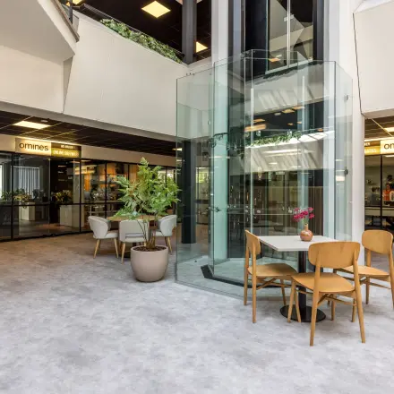 Bright and modern office area with seating and a central glass elevator, ideal for office space rental at Eindhoven Airport.