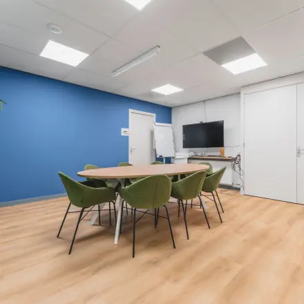 Bright office space for rent in Eindhoven Center with modern furniture, blue accent wall, and flat-screen TV, ideal for meetings.