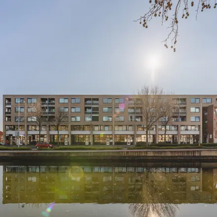 Exterior view of office building at Kanaaldijk-Zuid 19, Eindhoven Center, suitable for office space rental, with canal reflection and clear sky.