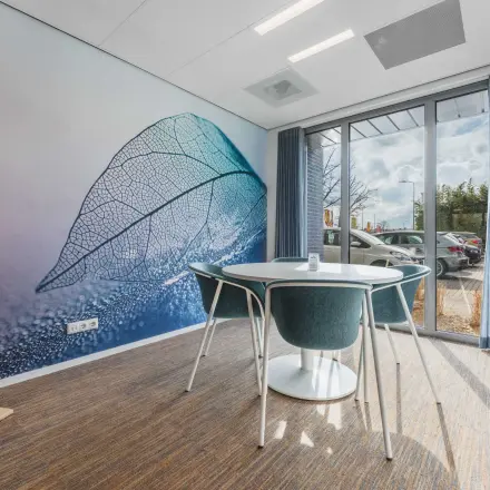 Bright office space with a large window, blue curtains, a wall mural, round table, and chairs for office space rental.