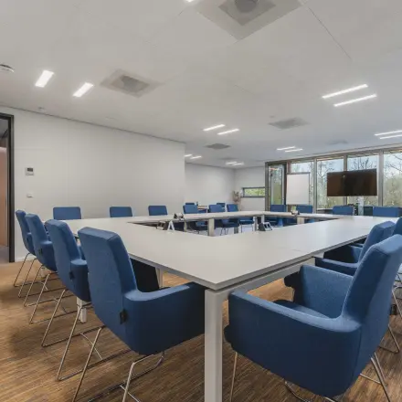 Spacious conference room with a large table surrounded by blue chairs, ideal for office space rental at Hurksestraat 60, Eindhoven De Hurk.