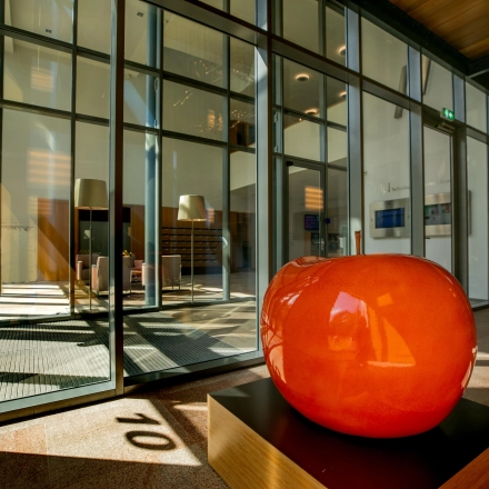 Modern office entrance at High Tech Campus 10, Eindhoven with large glass panels and vibrant orange sculpture, ideal for office space rental.