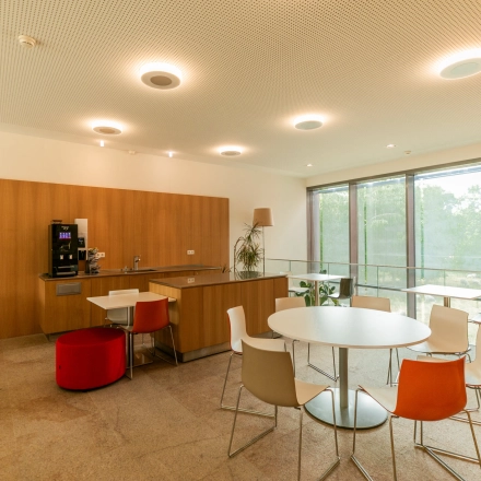 Modern office space rental at High Tech Campus 10, Eindhoven, featuring a bright, open lounge area with tables, chairs, and a coffee machine, perfect for informal meetings or a quick break.