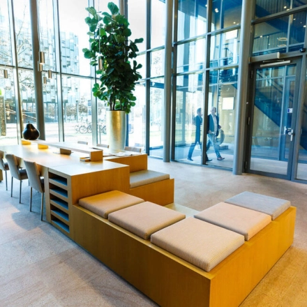 Modern office lobby at High Tech Campus 9, Eindhoven, with large windows, sleek wooden seating, and lush greenery. Ideal for businesses seeking office space rental.