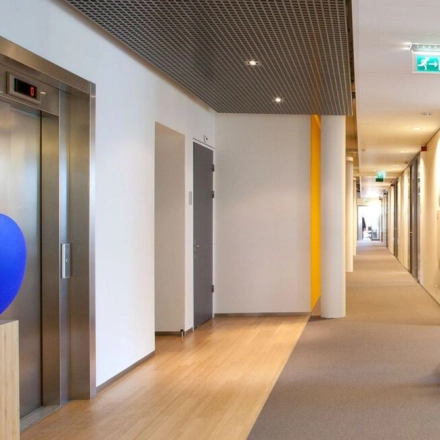 Modern hallway at High Tech Campus 9, Eindhoven, featuring sleek decor and efficient layout. Ideal for office space rental, combining functionality with a clean design. A person walks down the corridor, adding dynamic movement.