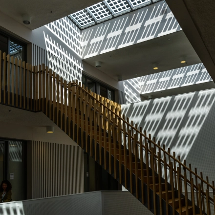 Interior view of a modern office space at TU campus, De Lismortel 31, Eindhoven High Tech Campus. Featuring geometric shadows and a wooden staircase, ideal for office space rental.