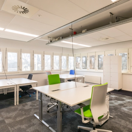 Modern office space rental at TU campus, Eindhoven High Tech Campus, featuring spacious work desks and ergonomic chairs in a bright, window-lined room.