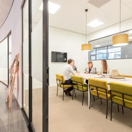 Interior view of a furnished office space rental at Anderlechtstraat 15, Eindhoven North, featuring a meeting room with three people engaged in discussion around a long table.
