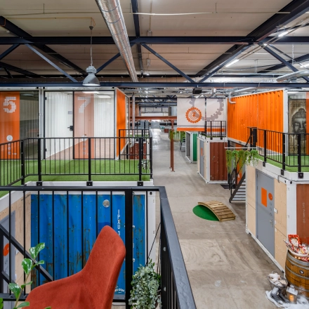 Colorful, creatively designed interior at Tarasconweg 2, Eindhoven North, featuring vibrant shipping container workspaces available for rent. Modern industrial style with open flooring and vibrant accents.