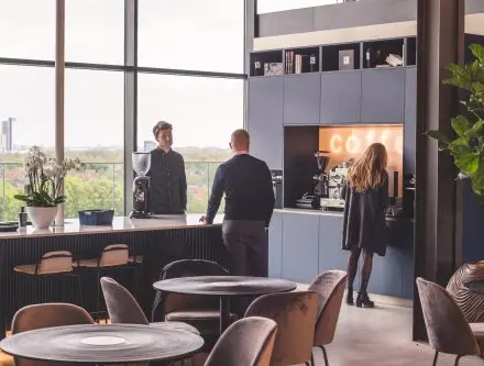 Modern furnished office space at Achtseweg Zuid 159R, Eindhoven Strijp-S, featuring people engaging in conversation by a coffee station.