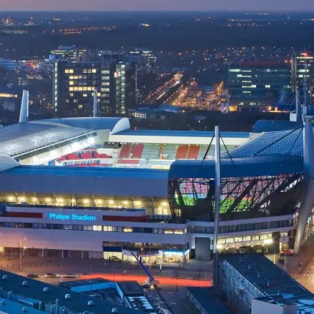An evening aerial view of the Philips Stadium in Eindhoven, showcasing the surrounding city lights and structures.