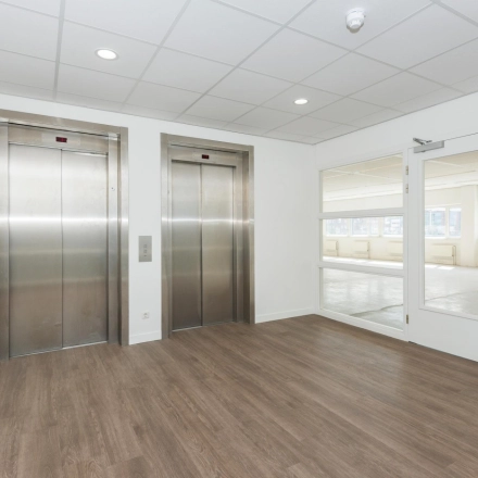 Interior view of office building at Brandweerstraat 20-30, Enschede featuring modern wood flooring and two sleek elevators, ideal for office space rental.