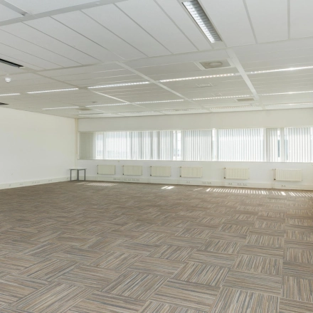 Spacious unfurnished office interior with neutral carpet and large windows, suitable for office space rental at Brandweerstraat 20-30, Enschede. Abundant natural light enhances the open, professional environment.