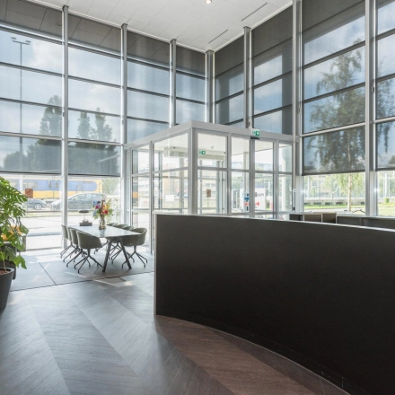 Spacious office entrance with large windows, sleek reception desk, and potted plants at Brandweerstraat 20-30, Enschede. Ideal for businesses seeking professional office space rental.