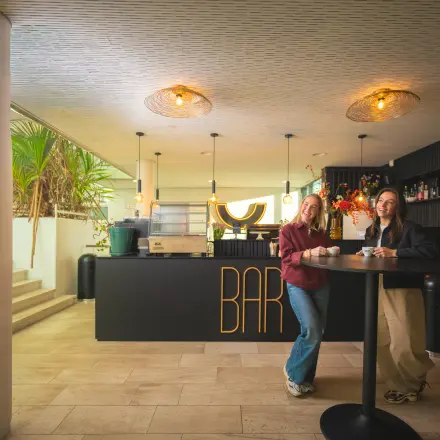 Two people enjoying drinks at a modern bar area near stairs, located in Brouwerijstraat 1, Enschede, ideal for office space rental.