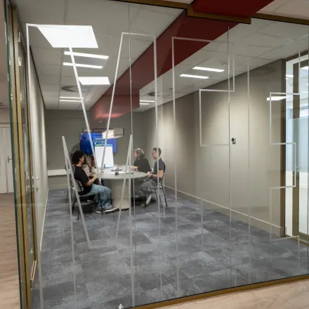 Glass-enclosed meeting room at Kuipersdijk 2-4, Enschede, with people engaged in a business discussion. Ideal for office space rental.