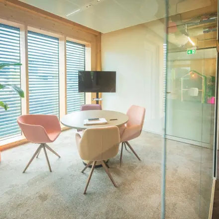 Inviting office space in Enschede with modern furnishings, featuring a round table and chairs near a window, ideal for office space rental.