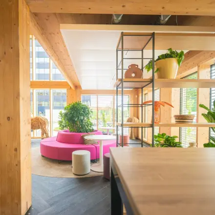 Bright, modern office space at Moutlaan 1-23, Enschede with wooden beams, vibrant seating, and open shelving. Ideal office space rental for dynamic work settings.