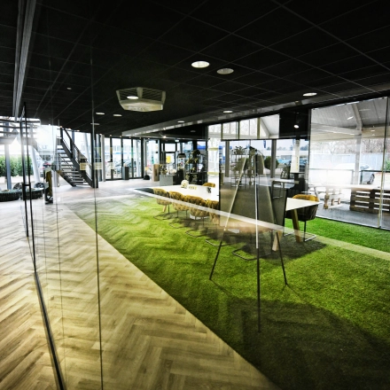 Spacious and modern office space with large windows and green flooring. Ideal for office space rental at Parkweg 102, Enschede. Features a meeting area and sleek design.