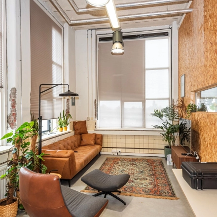 A cozy office to rent in Enschede features a comfortable seating area with leather chairs, a sofa, and a decorative rug, surrounded by indoor plants.