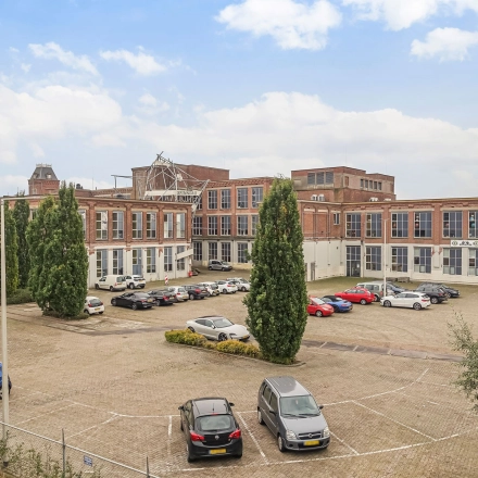 Exterior view of office spaces for rent at Rigtersbleek-Zandvoort 10, Enschede, featuring a spacious parking area with cars.