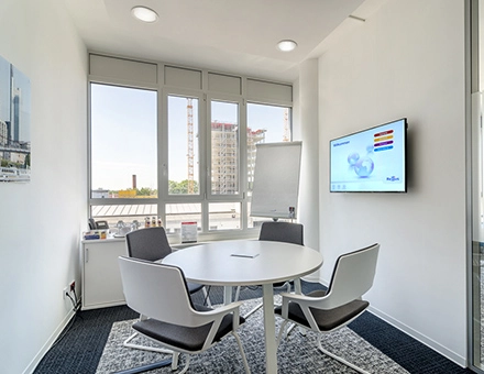 Bright office space with a round table and chairs, located at Mergenthaler Allee 15-21 in Eschborn, ideal for office space rental with large windows offering city views.