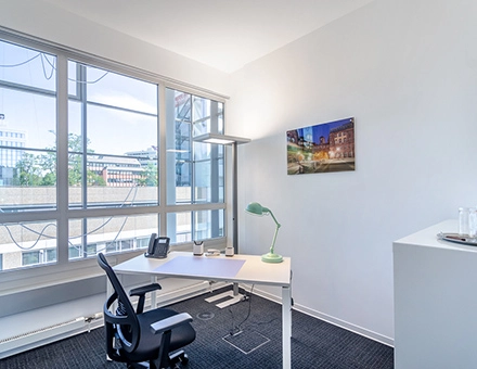 Bright office space at Mergenthaler Allee 15-21 in Eschborn with a desk and chair near large windows, ideal for office space rental.
