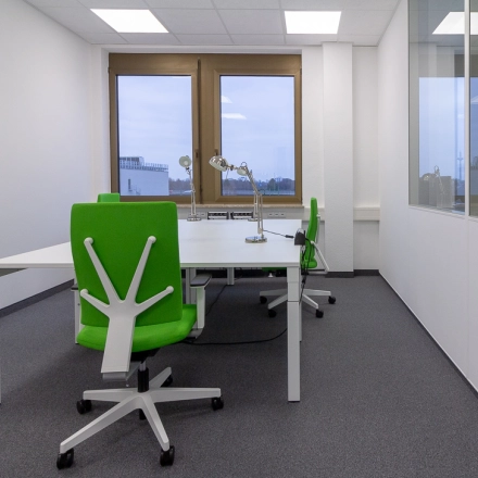 Modern office space rental in Frankfurt West with large windows, stylish green chairs, and desks for collaborative work.
