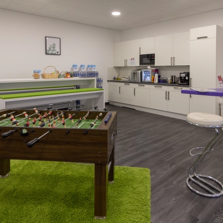 Bright office space featuring a foosball table, kitchenette with white cabinets, and bar seating area located in Frankfurt West, perfect for an office space rental.