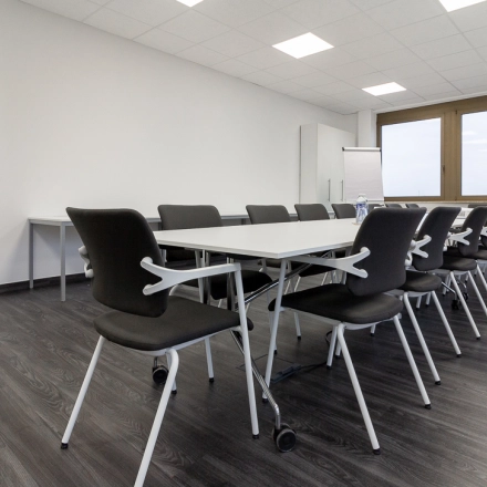 Spacious office to rent in Frankfurt West featuring a bright conference room with tables and chairs, ready for office space rental. Large windows provide natural light.