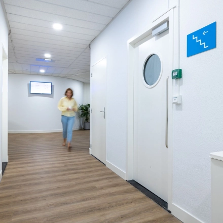 Bright hallway at Groningenweg 8 8, Gouda, suitable for office space rental, with a person walking towards a door, featuring wood-patterned flooring and minimal decor.