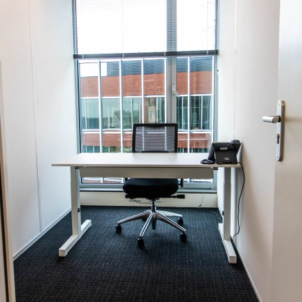 Compact office space for rent at Kampenringweg 45, Gouda, featuring a desk, chair, and a phone with window views.