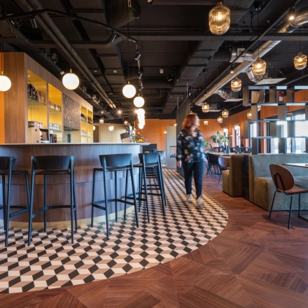 Modern office space in Gouda featuring a stylish bar area with seating, highlighting available office space rental at Zuidelijk Halfrond 1. A person is walking through the bright, welcoming environment.