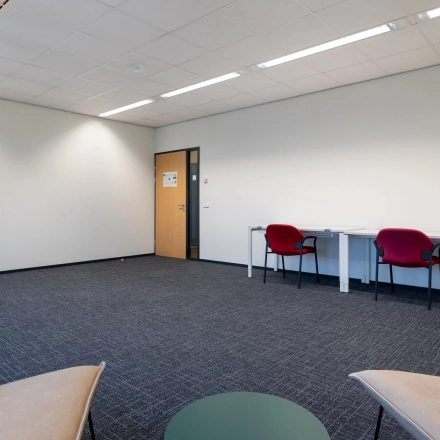 Spacious office for rent at Zuidelijk Halfrond 1, Gouda, featuring a minimalist design with carpeting, two desks, and chairs for a comfortable work setting.