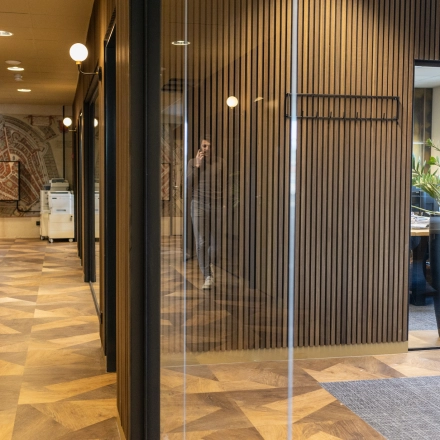 Modern office space at Zuidelijk Halfrond 1, Gouda, featuring wooden flooring, glass walls, and a well-lit interior with people engaged in business activities. Ideal for office space rental.