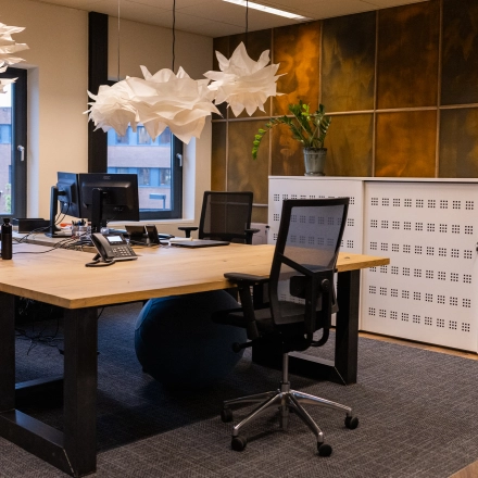 Modern office space in Gouda featuring workstations with computers, stylish lighting fixtures, and large windows creating a well-lit environment. Ideal for office space rental.