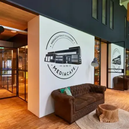 Inviting office space at Helperpark 270-298, Groningen featuring a cozy lounge with plush seating and stylish decor, ideal for meetings in this office space rental. Natural light illuminates the room through large windows.