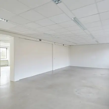 Spacious office space available for rental at Schweitzerlaan 12, Groningen, featuring a bright interior with large windows and neutral walls.