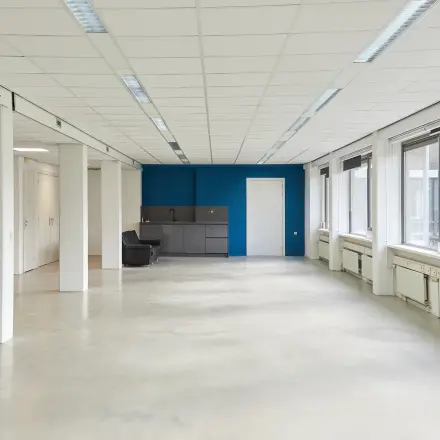 Bright, unfurnished office space at Schweitzerlaan 12, Groningen, featuring large windows and a small kitchenette area, perfect for office space rental.