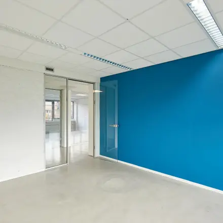 Bright empty office space with a blue accent wall and large windows in Groningen, ideal for office space rental at Schweitzerlaan 12.