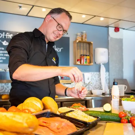 Individual preparing fresh sandwiches and salads in a modern office pantry at A. Hofmanweg 5A, Haarlem Waarderpolder. Ideal for entrepreneurs seeking office space rental with convenient amenities.